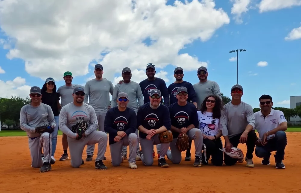 Employees from ABS and ABS Wind Miami, along with their families, gathered on a softball field during a company team-building and family event.