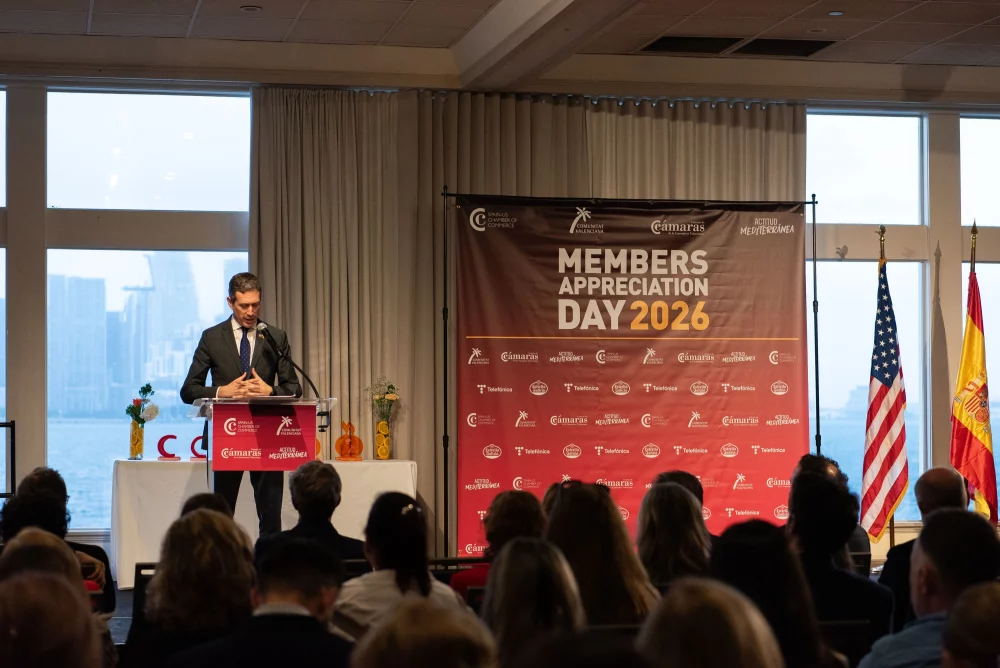 Speaker addressing attendees at the Spain-U.S. Chamber of Commerce’s Members Appreciation Day 2026 in Miami, with event branding and U.S. and Spanish flags displayed on stage.